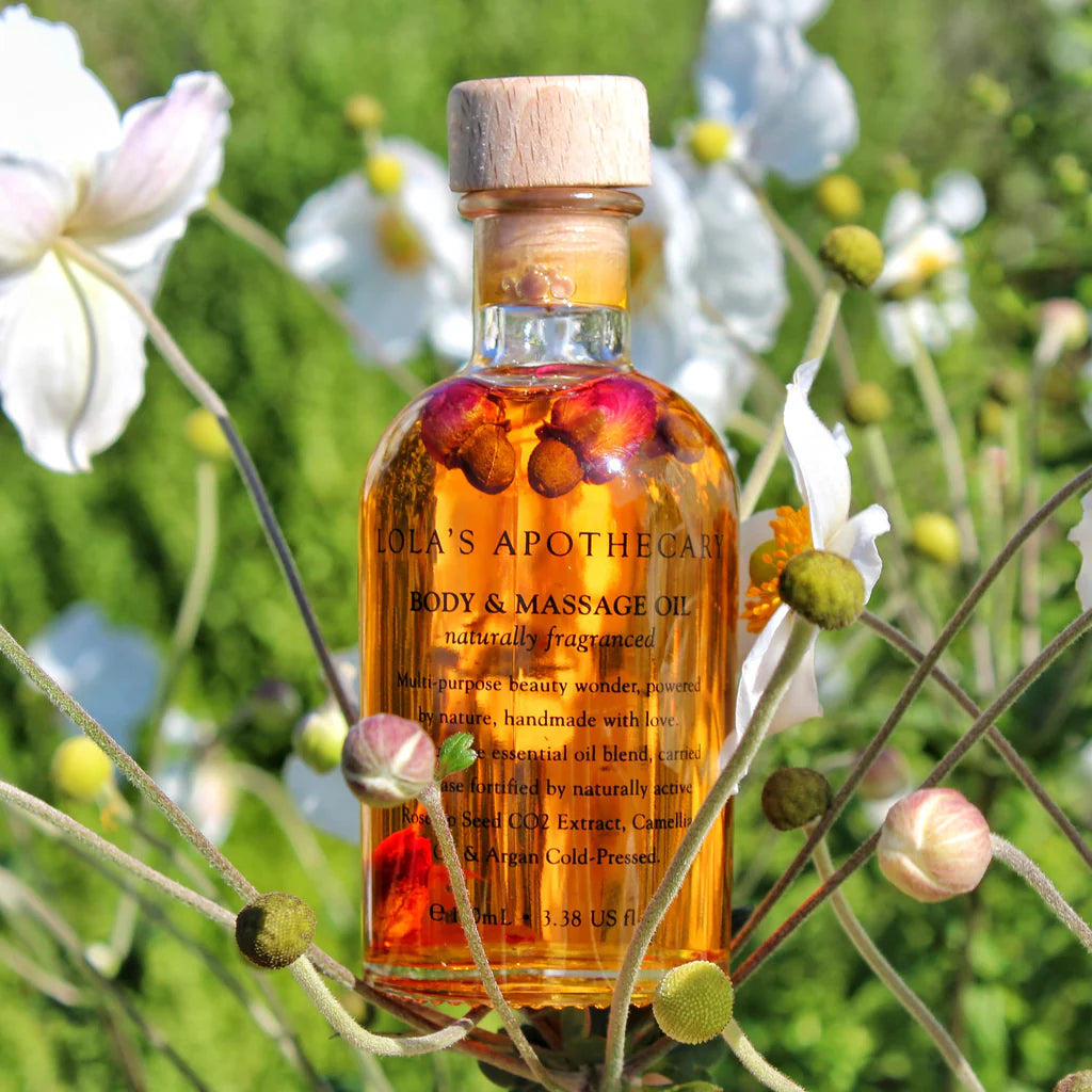 A bottle of "Divine Grace" regenerative body massage oil with outdoor floral background