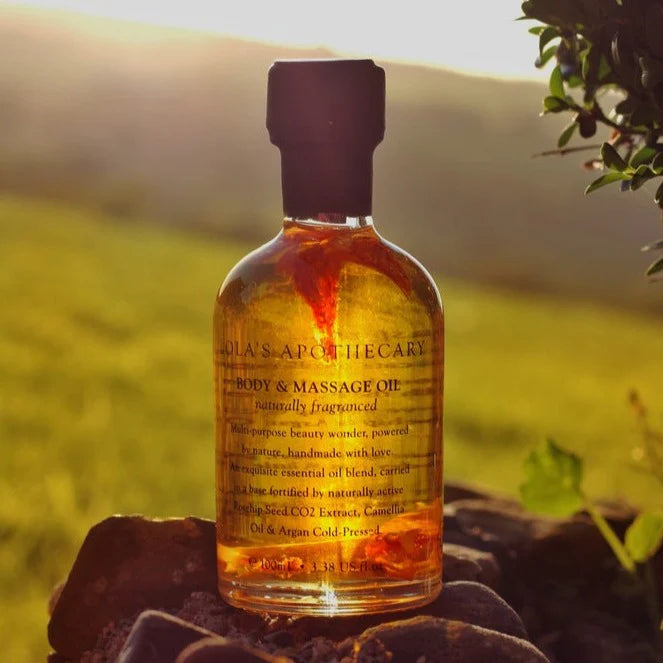 Bottle of Euphoric Indulgence body massage oil set on rocks with a green field  background