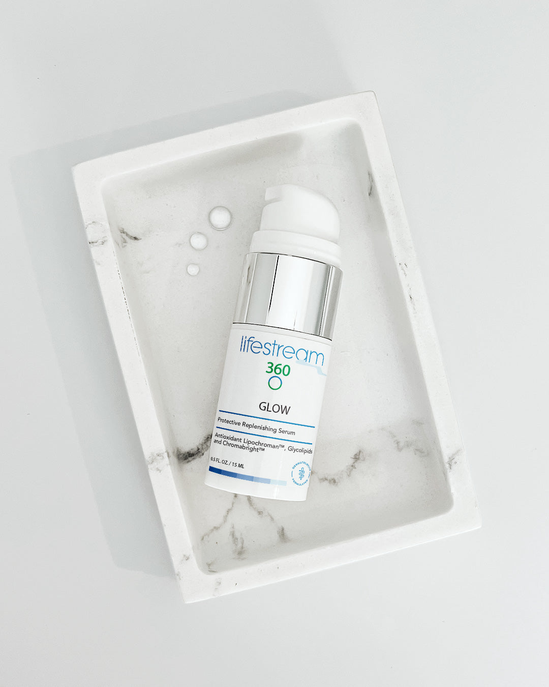 Travel size Bottle of Glow face serum in a white dish on a marble surface