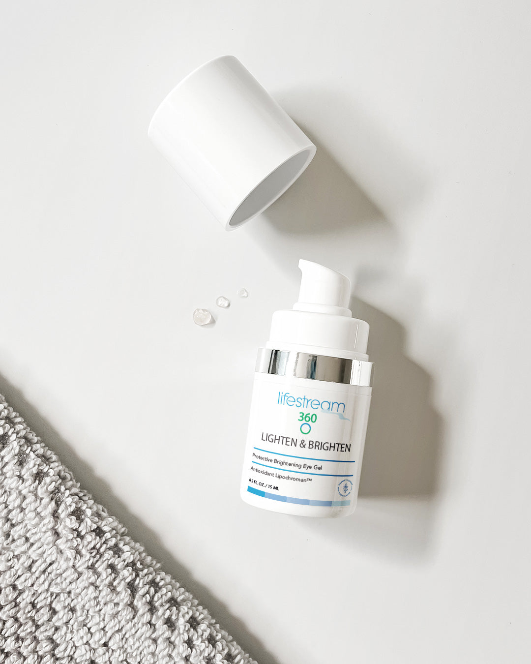 Lighten and Brighten eye gel bottle  on a white surface with a textured gray towel.