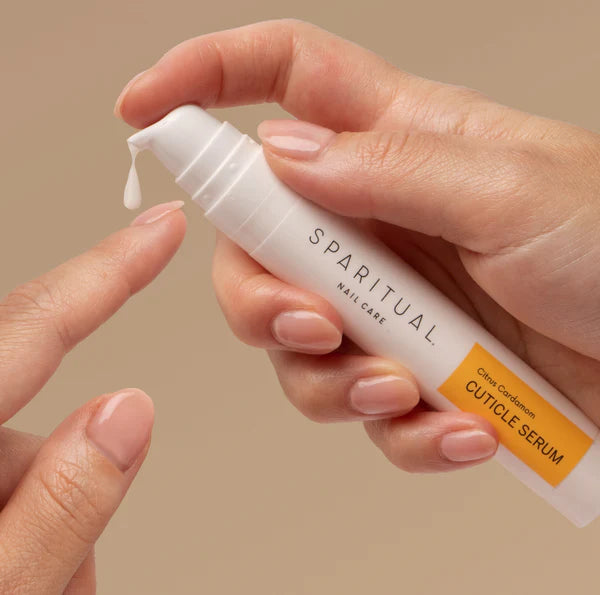 Hand holding a white bottle of Sparitual cuticle serum against a beige background