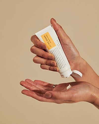 Hand applying hand cream from a tube against a beige background